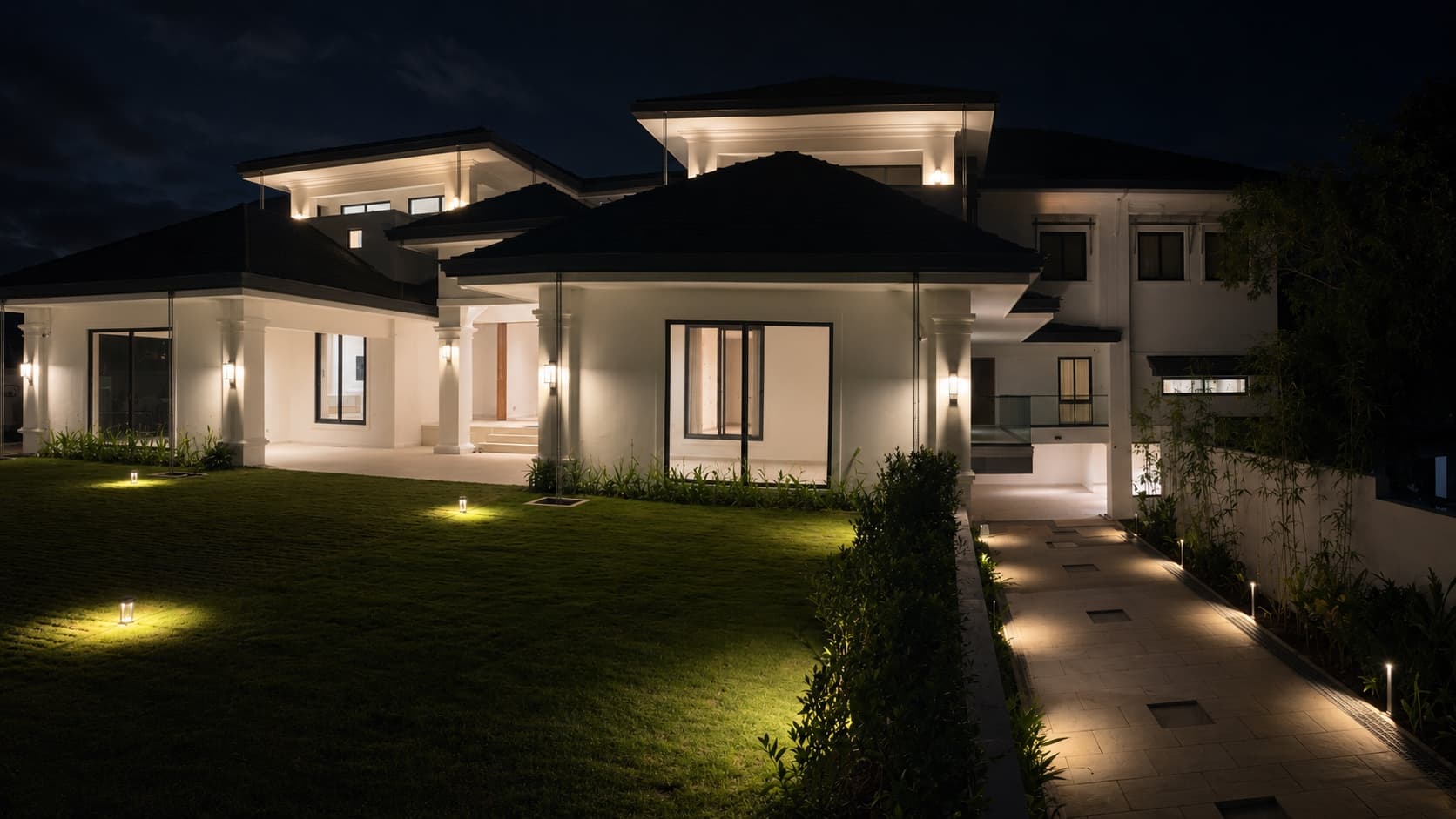 Chandranagar House at night — the lawn lit low, the white house glowing